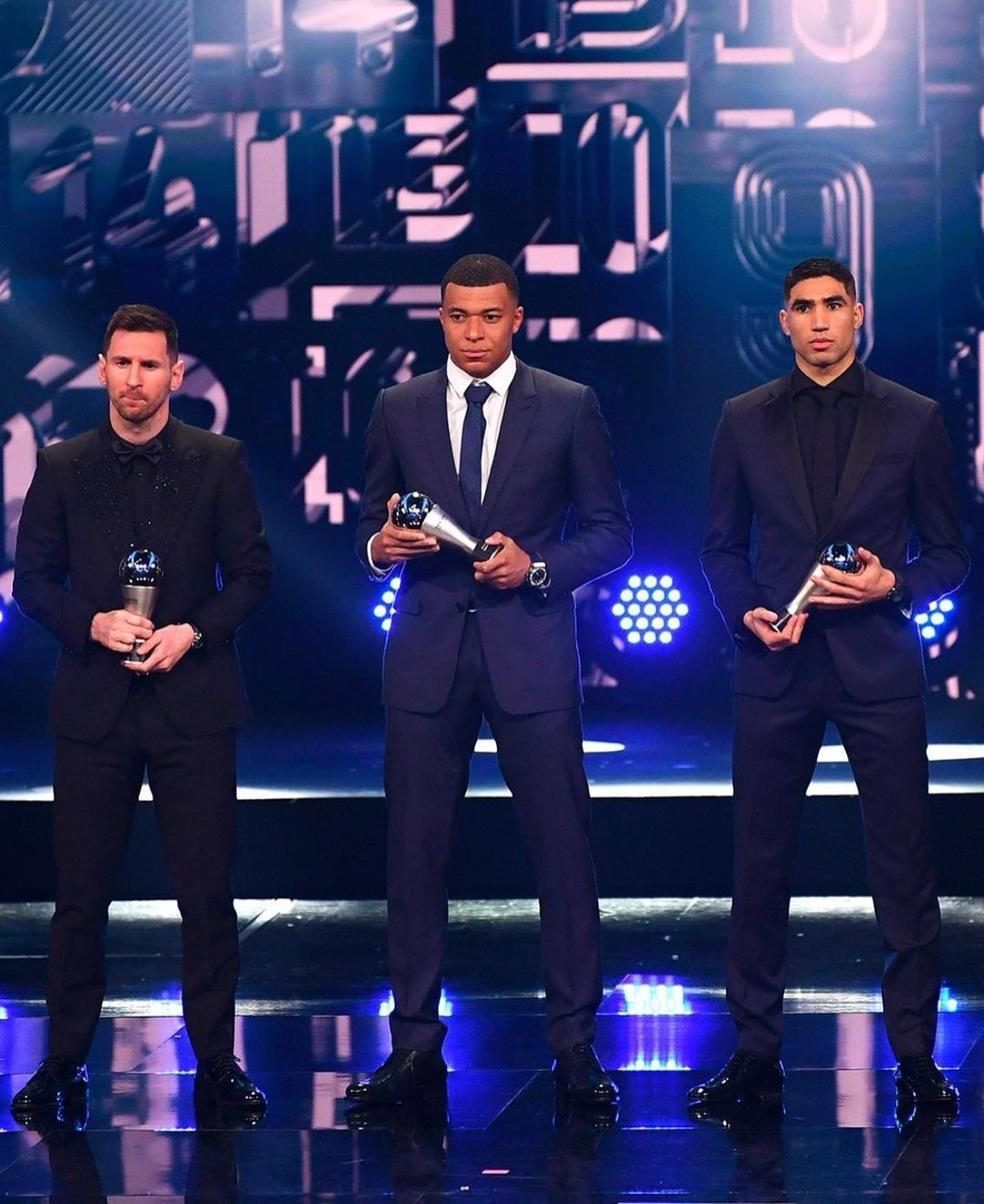 Tại lễ trao giải The Best 2022 hồi tháng 2, Kylian Mbappe diện sơ mi trắng, vest xanh đen, giày da bóng và đồng hồ Hublot. Cùng với Messi (trái) và Hakimi (phải), anh được vào danh sách đội hình cầu thủ nam xuất sắc thế giới.