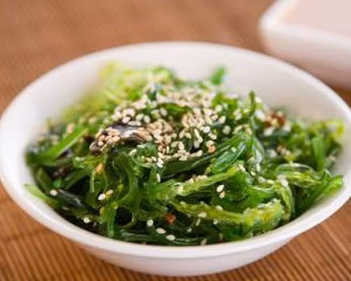 Salad rong biển. Nguyên liệu: Rong biển: 70g; Dưa chuột: 2 quả; Rau xà lách: 100g; Vừng trắng; Gia vị: Đường, muối, tiêu. Dưa chuột rửa sạch, bỏ ruột xắt lát, trộn một chút giấm và đường. Rong biển ngâm rửa sạch sau đó tước thành sợi nhỏ.Vừng rang đến khi vàng thì nhắc xuống. Trộn dưa chuột, rong biển với giấm, đường, muối sao cho vừa. Để ngấm trong 5-10 phút, xếp xà lách vào đĩa cho salad rong biển vào rồi rắc vùng lên trên.