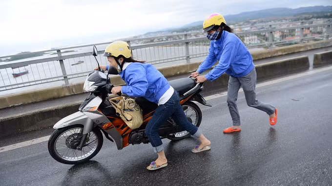 Bất chấp lệnh cấm xe máy đi qua cầu Bãi Cháy, một số người vẫn tìm cách qua cầu trong gió mạnh. Và đã có không ít xe ngã đổ dúi dụi trên cầu trong gió bão. Trong ảnh là 2 phụ nữ cố tình chạy xe qua cầu bị gió thổi ngã phải dắt bộ. Ảnh: Tuổi Trẻ.