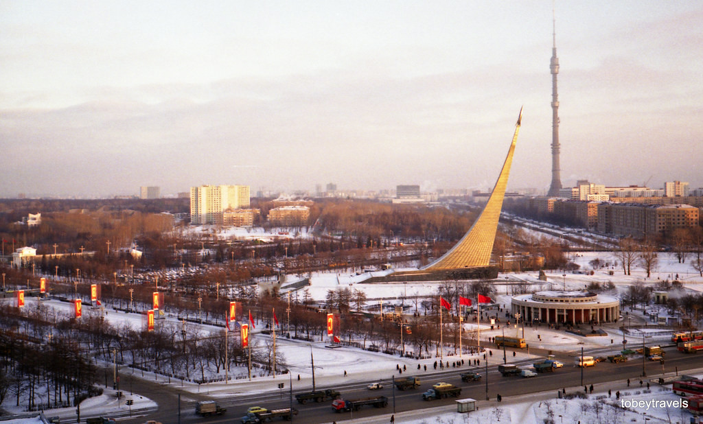 Tượng đài Chinh phục không gian bên lối vào khu triển lãm, nhìn từ khách sạn Cosmos. Phía xa là tháp truyền hình Ostankino.