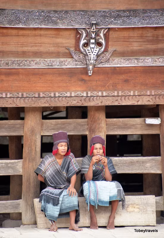Hai nam giới người Batak Toba ngồi bên ngoài nhà sàn.