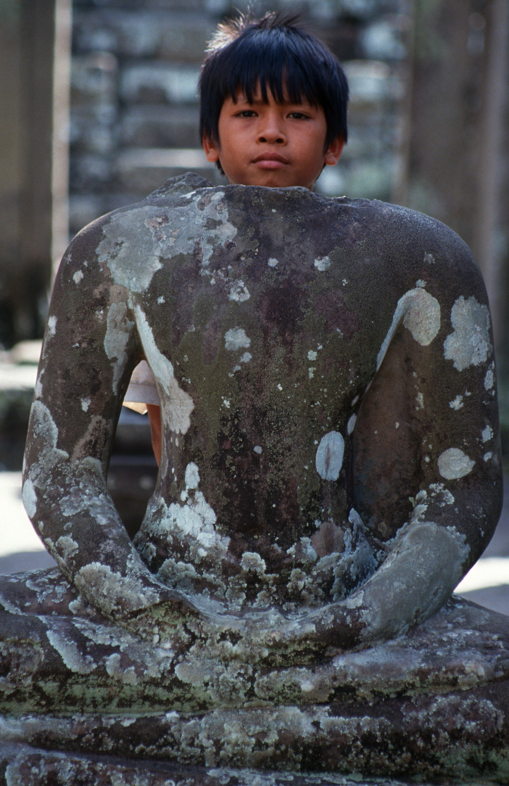 Cậu bé Campuchia sau bức tượng cụt đầu tại một ngôi đền cổ ở Siem Reap.