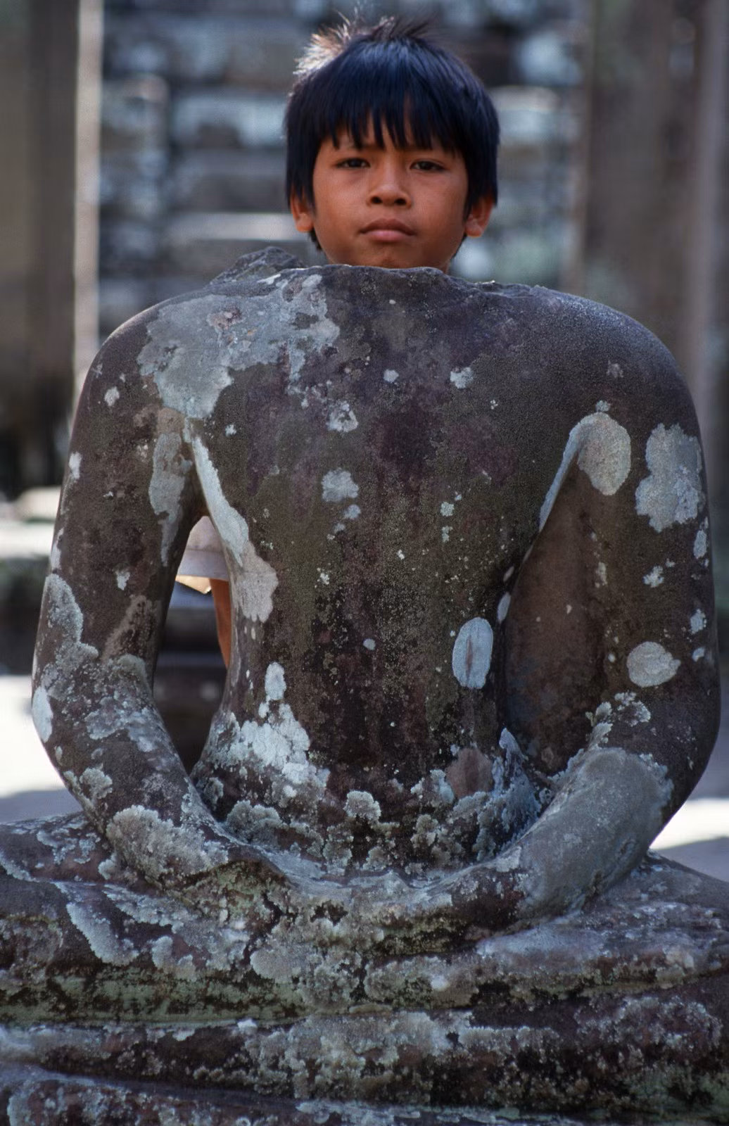 Cậu bé Campuchia sau bức tượng cụt đầu tại một ngôi đền cổ ở Siem Reap.