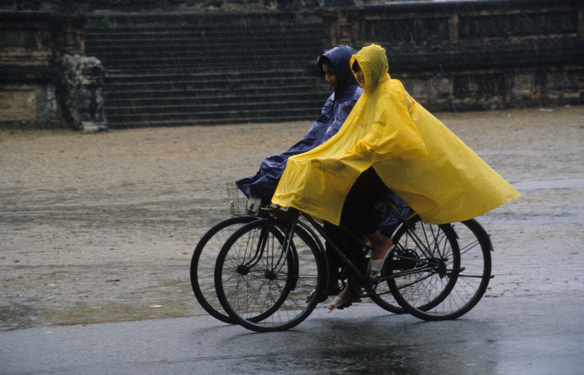 Hai nữ sinh đạp xe ngang qua Bia Quốc Học dưới cơn mưa tầm tã.