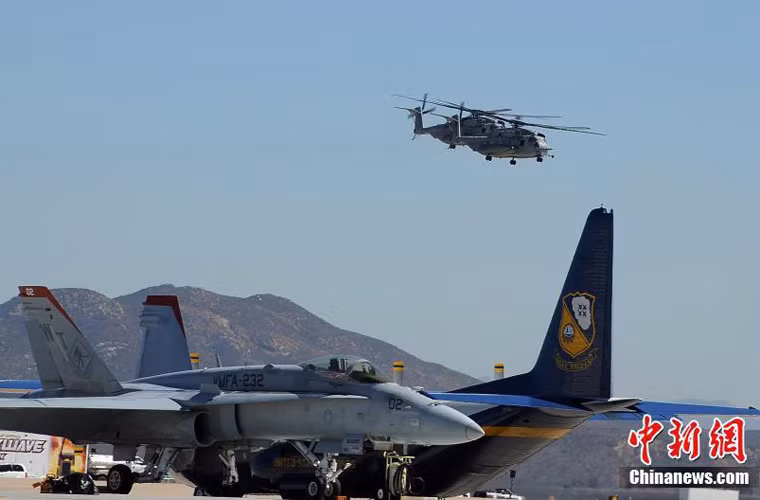 F/A-18C đậu cạnh chiếc vận tải cơ C-130 thuộc phi đội biểu diễn Blue Angels. Trên trời là các trực thăng vận tải hạng nặng CH-53 bay biểu diễn.