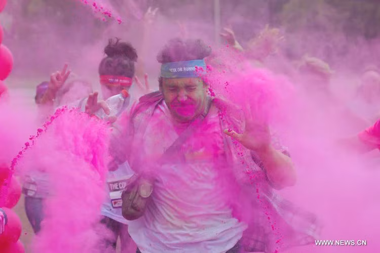 Một người đàn ông nhắm mắt và giơ cao 2 tay khi bị ném bột màu.