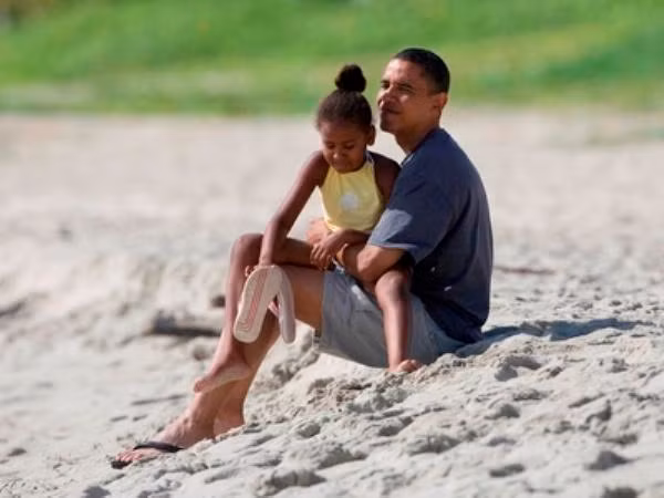 Như mọi người cha, Tổng thống Obama trông gần gũi và dịu dàng khi bế cô con gái thứ 2, Sasha trong lòng ngồi thư giãn trên bãi biển Kailua ở Kailua, Hawaii tháng 8/2008.