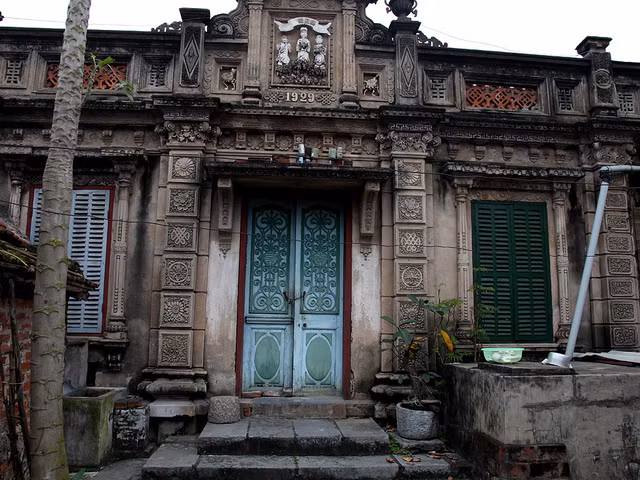 Trong ảnh là căn nhà được xây dựng từ những năm 1929 của cụ phó Du, nay là nơi gia đình ông B.V.K đang cư ngụ. Bậc thềm được xếp bằng những phiến đá ngay ngắn. Toàn bộ cột nhà được đắp nổi họa tiết hoa và tỉa cạnh rất tỉ mỉ.