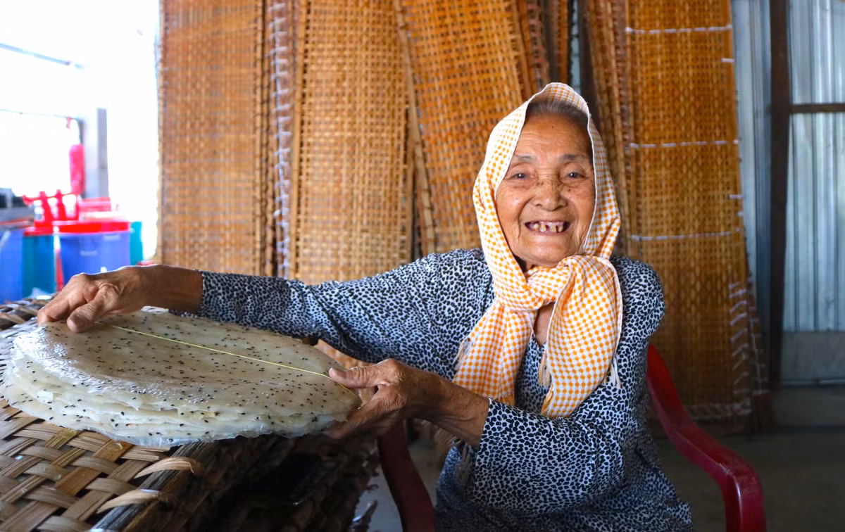 Có tuổi nghề hơn 30 năm, cụ Đỗ Thị Đượm (88 tuổi, ngụ phường Thuận Hưng) nhớ về những ngày khi mới khởi nghiệp nghề làm bánh tráng với nhiều thăng trầm. "Nghề này cực khổ lắm. Hồi đó, gia đình nghèo, tôi phải đi cắt lúa mướn, rồi ở lại mót lúa còn sót lại, bắt cá cạn để về làm mắm ăn. Sau đó, con dâu tôi mới dành dụm tiền xây được cái lò, rồi tôi và con gái cùng làm. Mấy chục năm trước tráng có cái Tết, mà chỉ tráng bánh tráng mặn thôi. Còn bây giờ tráng quanh năm, rồi con gái tôi mới tráng thêm bánh tráng lạt, bánh tráng ngọt và bánh tráng dừa. Nhu cầu của khách hàng ngày càng nhiều, gần đây nó đầu tư thêm máy tráng để kịp sản xuất cung ứng", cụ Đượm tâm sự - Ảnh: Kim Hà.