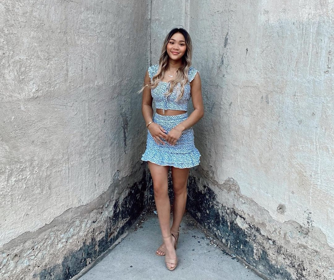 Ngoài quần dài, Sunisa Lee thường phối áo crop top xếp bèo nữ tính cùng chân váy đồng điệu chất liệu và họa tiết. Với kiểu trang phục này, nữ vận động viên chọn giày cao gót tông màu nude để tạo hiệu ứng đôi chân thon gọn.