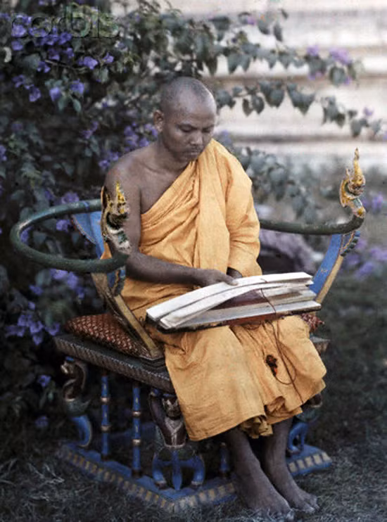 Một nhà sư ngồi trên chiếc ghế chạm khắc cầu kỳ, cầm trên tay những bản kinh cổ.