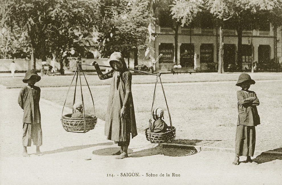 Một bà mẹ gánh hai con nhỏ bằng đòn gánh ở Sài Gòn.