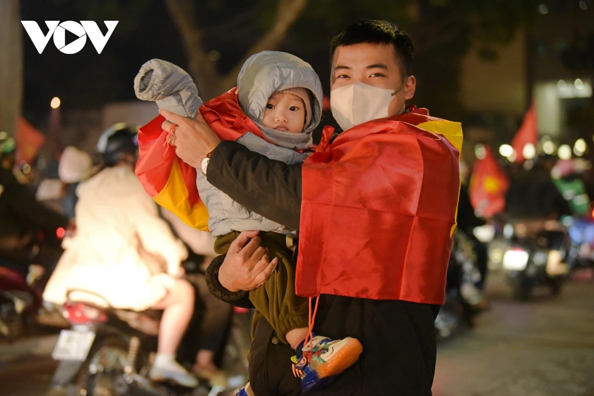 Một em bé đi theo bố đã buồn ngủ nhưng có thể thấy bố em bé vẫn rất sung, hăng hái cổ vũ ăn mừng chiến thắng.