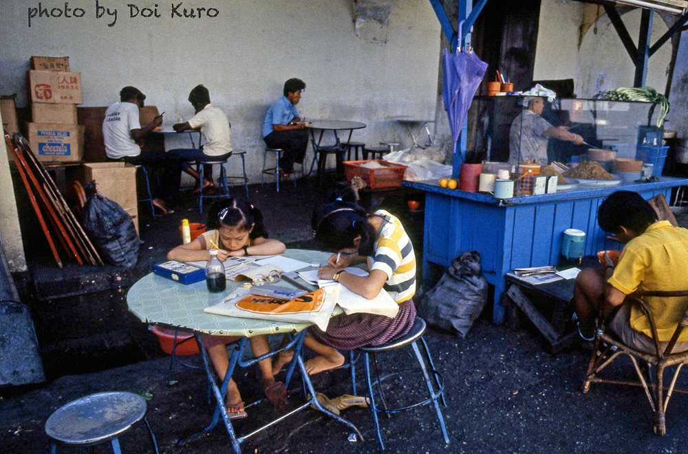 Hai cô bé làm bài tập về nhà trên chiếc bàn của quán ăn đường phố.