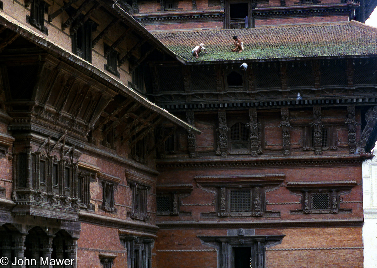 Hai người đàn ông đang cọ rêu trên mái ngói của một công trình cổ.