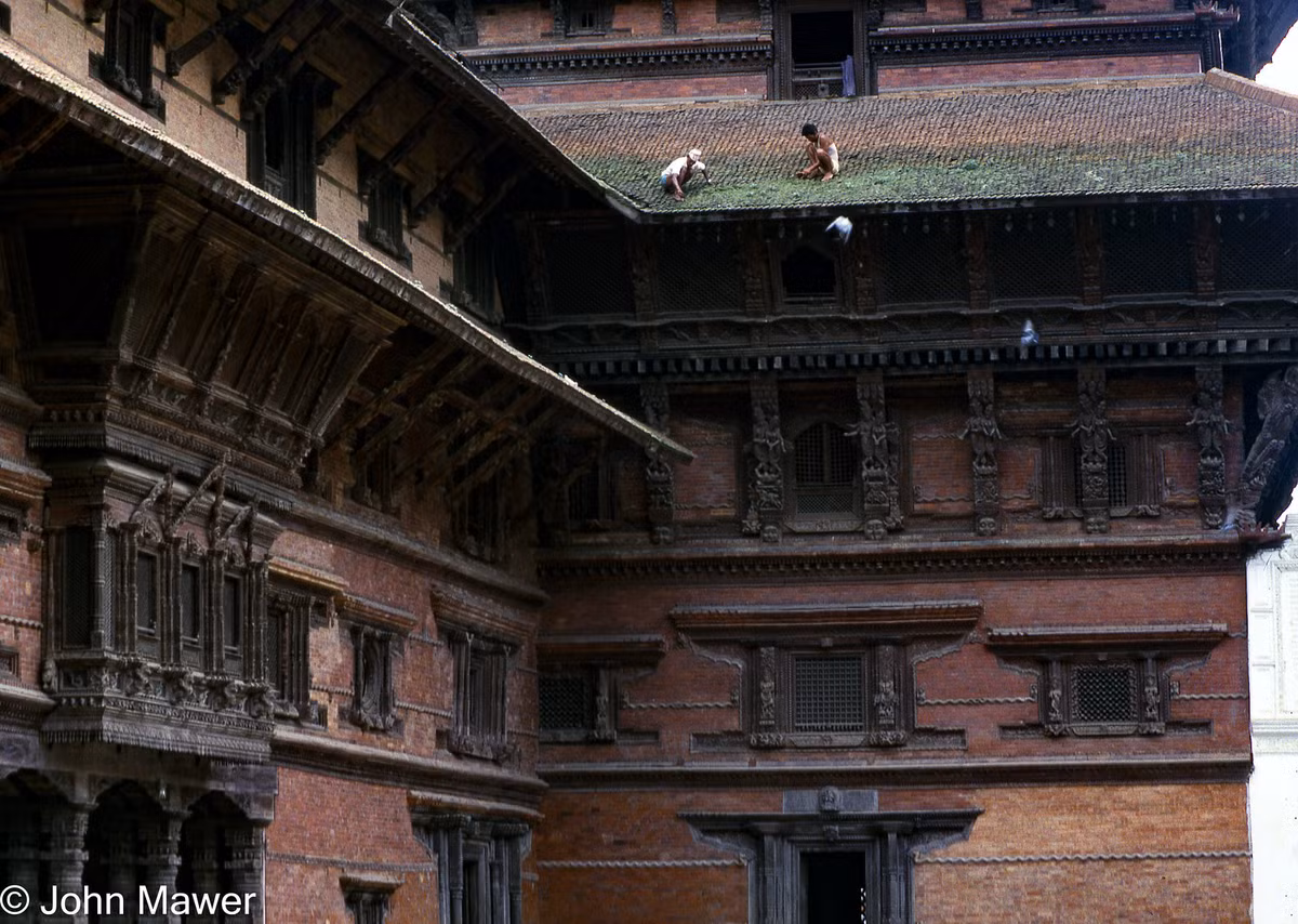 Hai người đàn ông đang cọ rêu trên mái ngói của một công trình cổ.