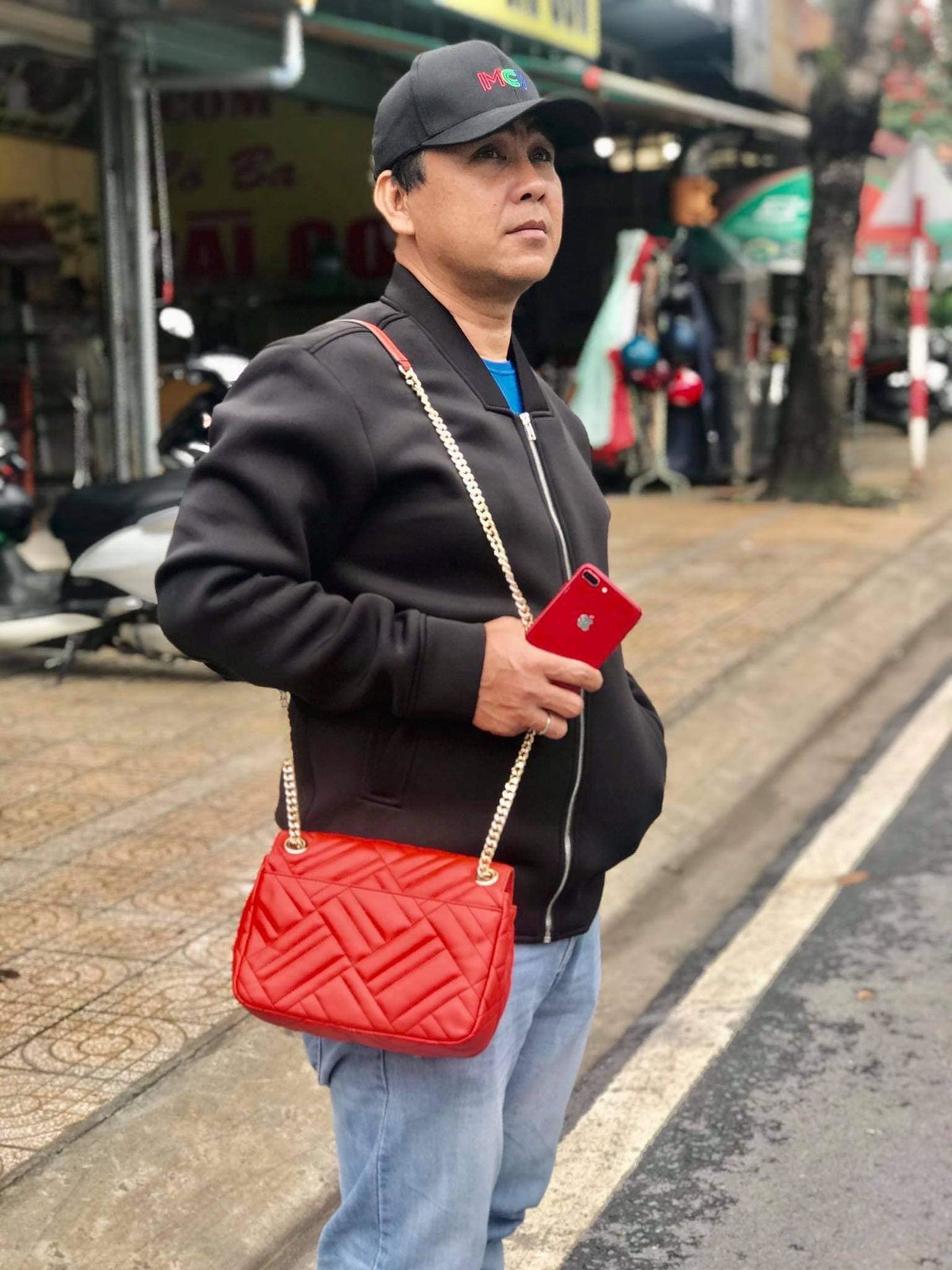 Quyền Linh tạo dáng chụp ảnh hài hước khi khoác túi xách cho vợ.