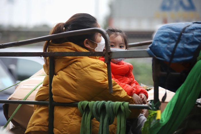 br/> Bé gái ngồi với người thân sau chiếc xe ba gác cùng nhiều đồ đạc. Xe mắc kẹt tại đoạn ùn tắc, bé thi thoảng gục vào người phụ nữ đang bế.