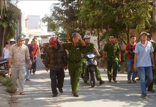 Thượng tá Sâm (bìa phải) đang "dìu" tên Long (đội mũ BH đỏ) rời khỏi hiện trường, đưa ra xe về trụ sở công an quận 9 để lập hồ sơ xử lý.