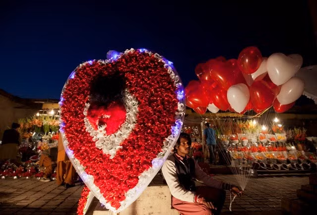 Một chàng trai trẻ ngồi bán bóng bay và hình trái tim khổng lồ bằng hoa giấy tuyệt đẹp một ngày trước Valentine ở Islamabad, Pakistan.
