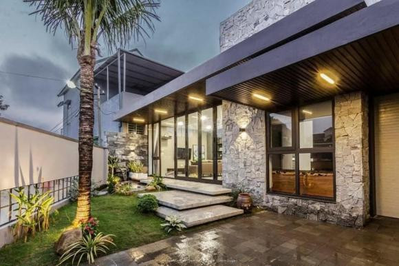 Tận dụng mảnh đất méo trước nhà, gia chủ làm khuôn viên vườn và bể cá. Sân và tiểu cảnh đều được ốp bằng đá tự nhiên, tạo cho ngôi nhà có màu sắc tự nhiên và gắn kết với các không gian còn lại. Để giải phóng tầm nhìn, nhóm thiết kế sử dụng nhiều hệ cửa kính lớn. Điều này, tạo ra một không gian sinh hoạt mở, gần gũi với thiên nhiên.