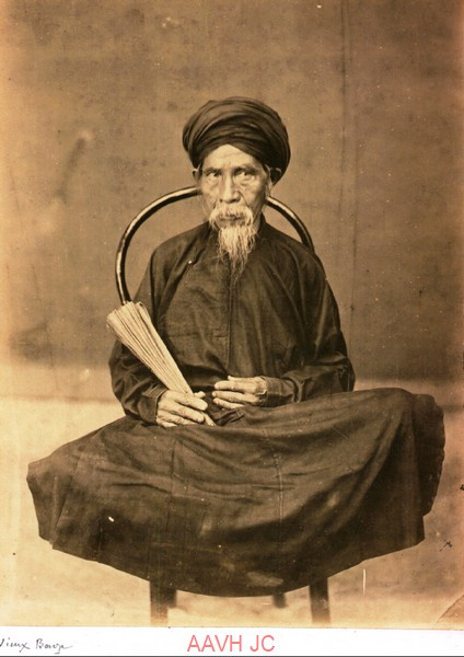 Cụ ông ngồi khoanh chân trên ghế.