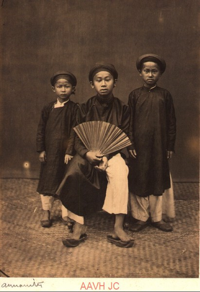 Người anh ngồi ghế và hai cậu em đứng bên cạnh.