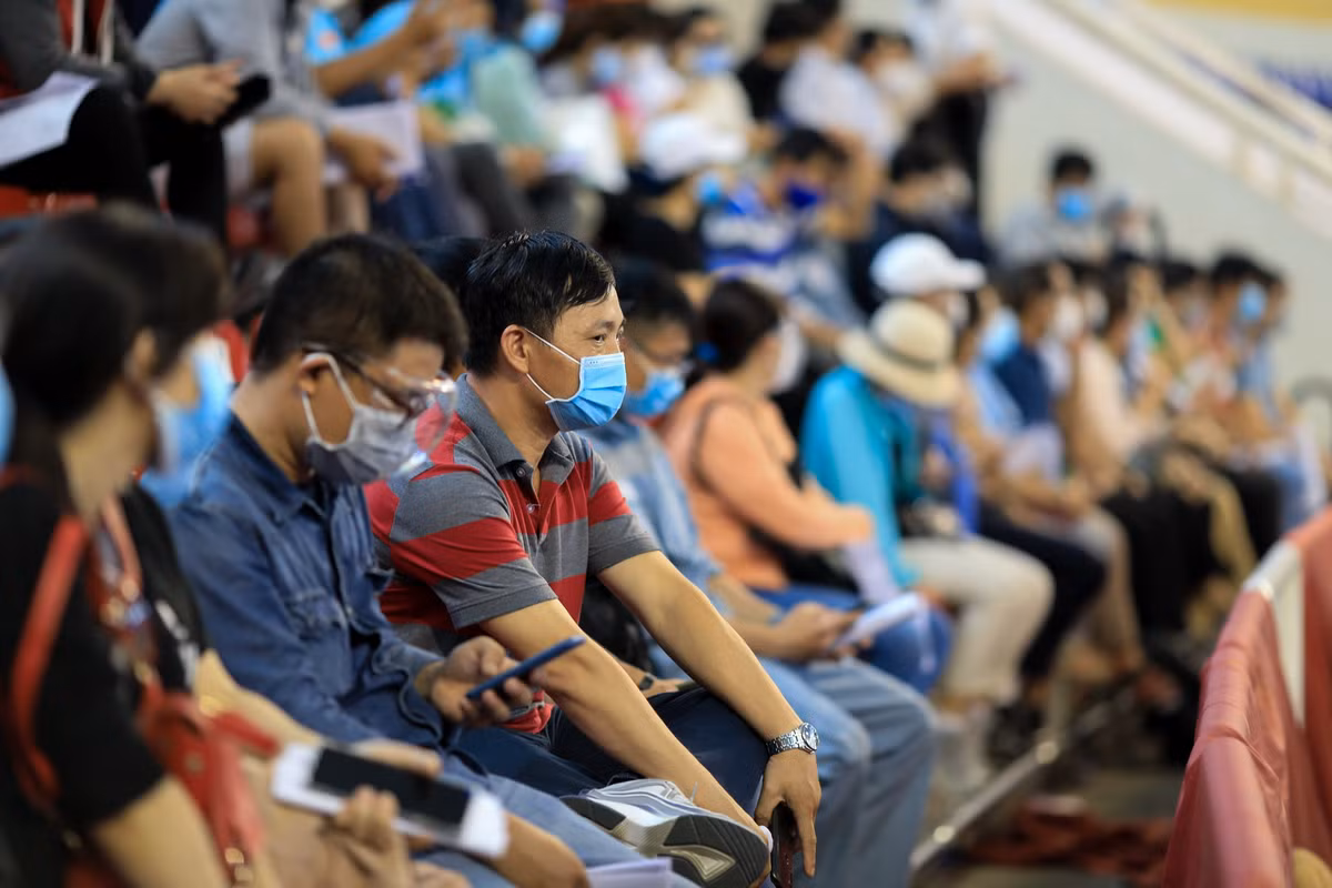 Số lượng người chờ tiêm quá đông, nhiều khu vực trên khán đài người dân phải ngồi sát nhau không đảm bảo khoảng cách tối thiểu 1,5 mét. Anh Đặng Văn Thuận (áo xám đỏ), nhân viên công ty điện lực ở Bà Rịa - Vũng Tàu, ngồi chờ trên khán đài gần 3 giờ nhưng vẫn chưa được gọi tên. "Nhìn thấy cảnh đông đúc thế này tôi rất lo lắng vì ngồi gần nhau quá, sợ chưa kịp chích vaccine Covid-19 đã bị nhiễm bệnh", anh Thuận chia sẻ.