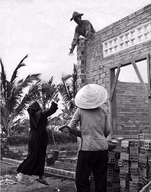 Nữ tu sĩ ở trung tâm trẻ mồ côi Bình Lợi ném gạch lên trên cho các công nhân trong thời gian xây dựng lớp học mới cho trẻ em năm 1969.