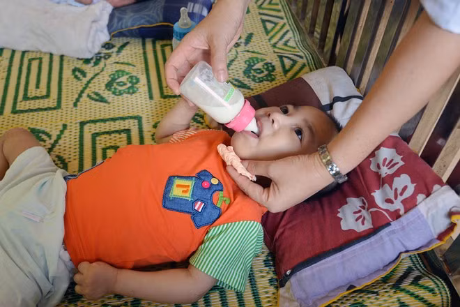 Một em nhỏ được nhân viên trung tâm cho bú sữa và chăm sóc cẩn thận.