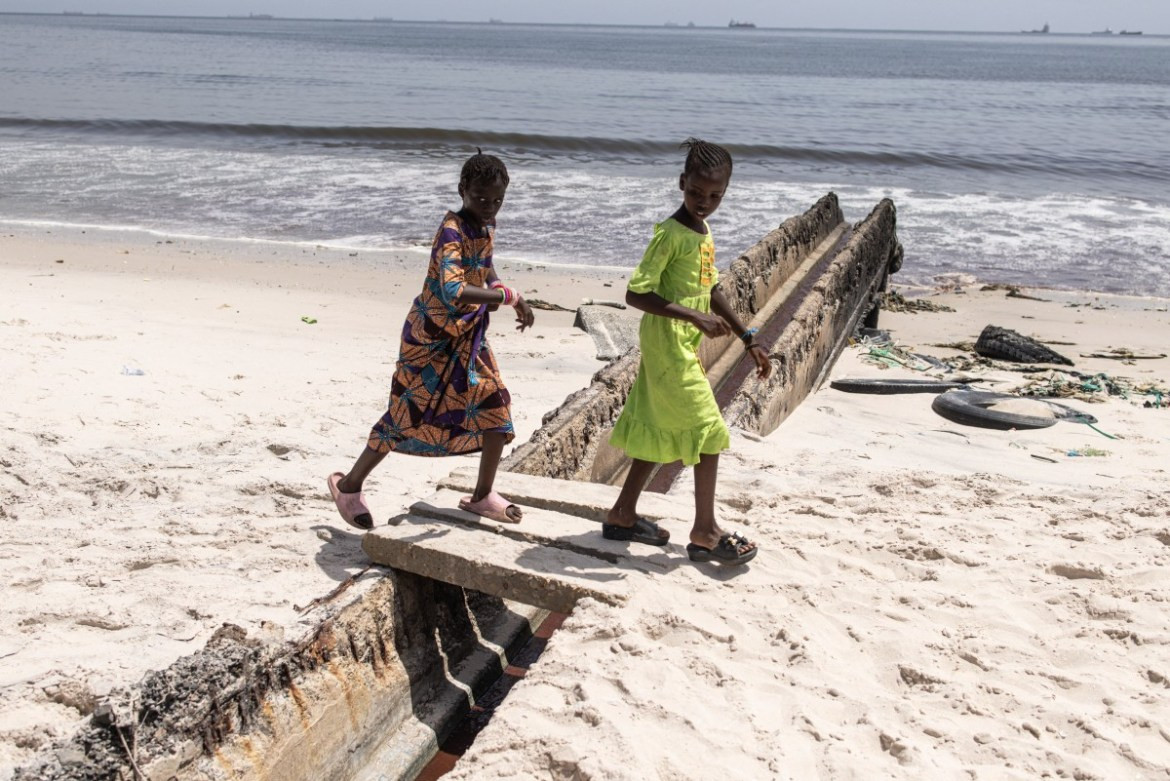 Hai bé gái đi qua một con kênh dẫn nước thải chảy ra biển ở Dakar.