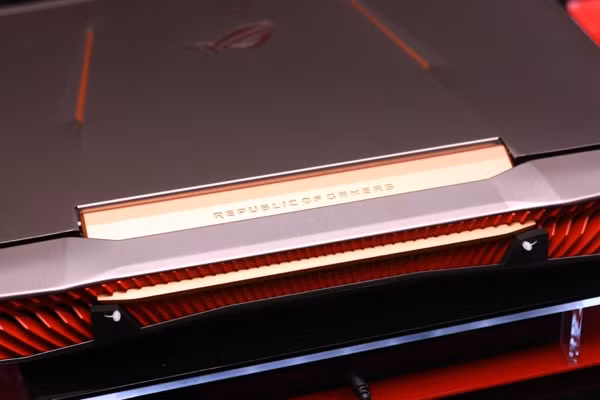 Thân máy có vỏ nhôm mài xước màu xám, với các chi tiết màu đỏ, cam.