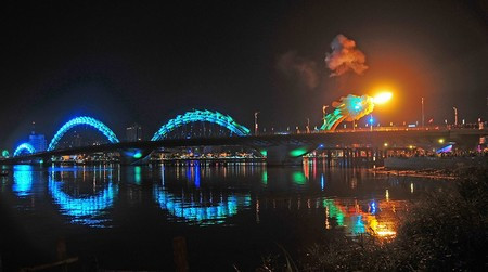 Thân Cầu Rồng tỏa ánh sáng màu xanh nước biển khi đang phun lửa trong đêm.