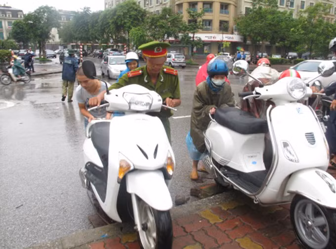 Chiến sĩ Đồn Công an số 1 , Công an huyện Từ Liêm giúp dân đưa xe lên vỉa hè để qua chỗ ngập. Ảnh: Người Lao Động