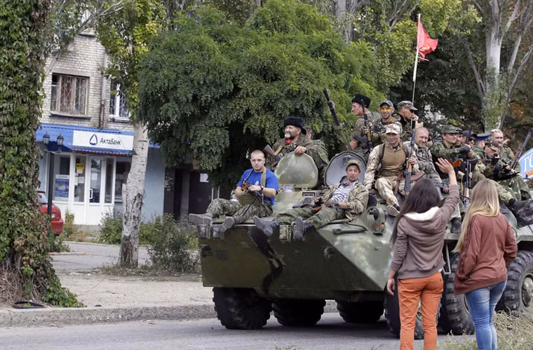 Một nhóm dân quân với đủ kiểu quân phục, vũ khí ngồi trên xe thiết giáp chở quân BTR-80 đang được các cô gái chào đón.