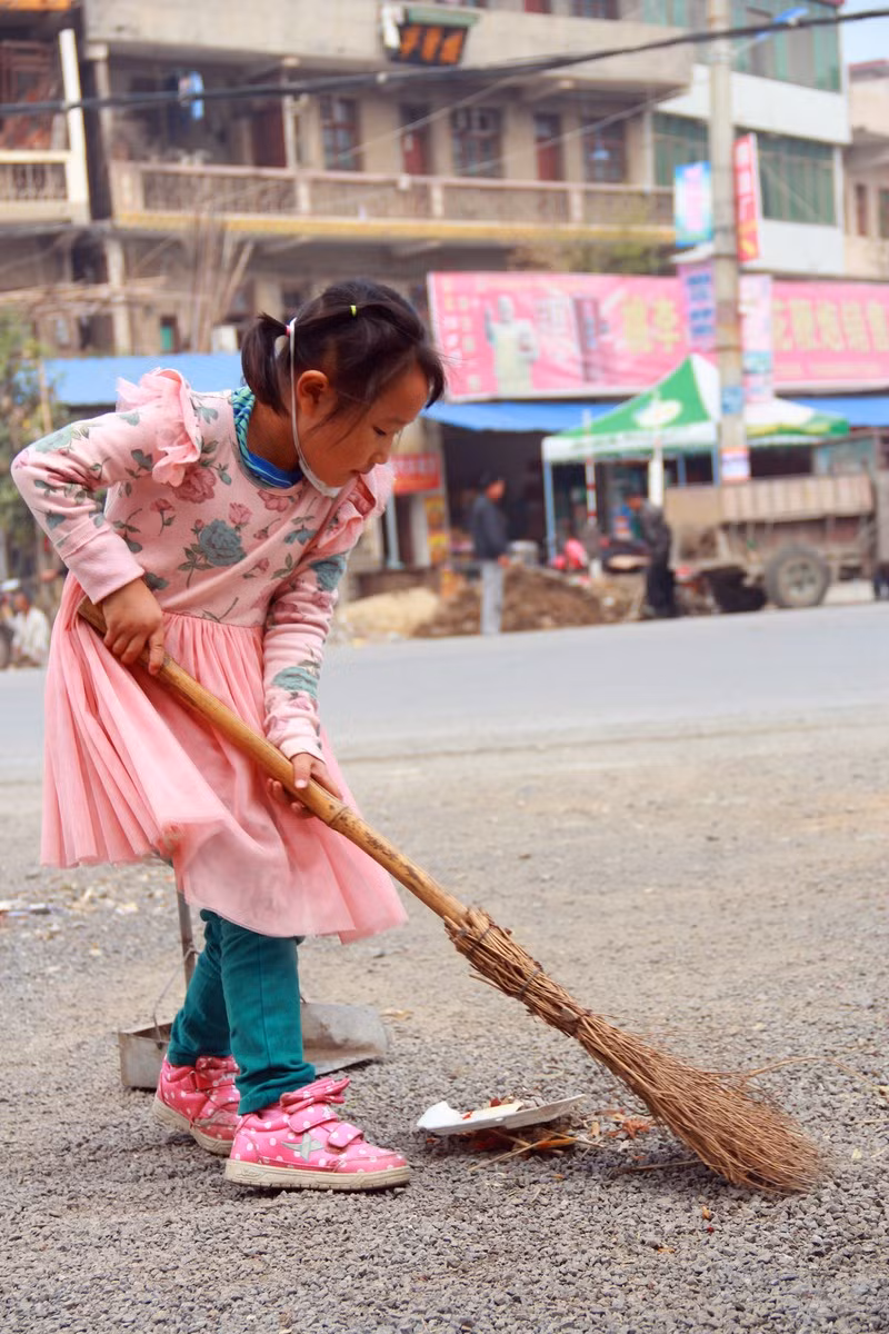 Mỗi cuối tuần, cô bé 5 tuổi lại ra lề đường gần nơi hai bà cháu đang sinh sống, làm thuê để quét dọn. Cô bé dáng người nhỏ xíu nhưng cũng biết cầm chổi, xẻng quét dọn rất sạch sẽ.