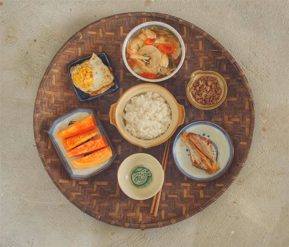 "Nhiều bữa mình cũng hay kết hợp một vài thứ với nhau, thấy ăn cũng ngon. Mấy món mình nấu đơn giản, ở quê có lẽ quen lắm rồi ấy bởi tuổi thơ ai cũng từng ăn", Ngoan nói. Trong hình, mâm cơm quê giản dị gồm canh măng chua, trứng ốp, cá khô rán và thịt chưng mắm tép. Ngoài ra còn có đu đủ chín cây hái trong vườn nhà.