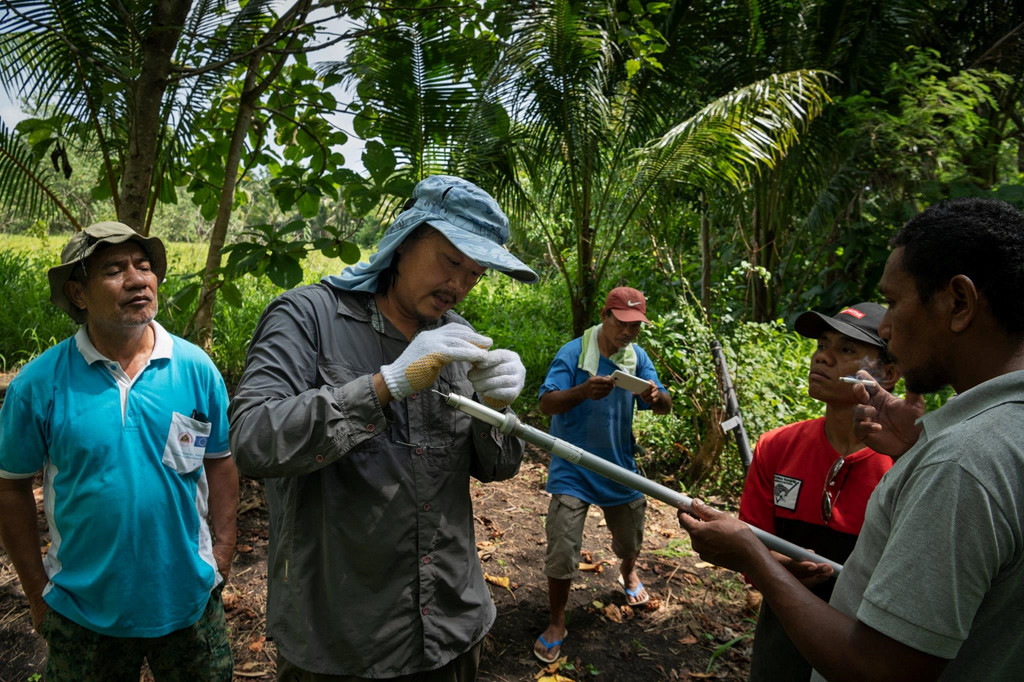 Nhà nghiên cứu Yusuke Fukuda (giữa) kiểm tra mẫu ADN do Victorino De Araujo (phải), mặc áo màu xám, một người địa phương làm lính cứu hỏa nhưng được biết đến trong thị trấn là người có thể gọi tới khi bị cá sấu tấn công.