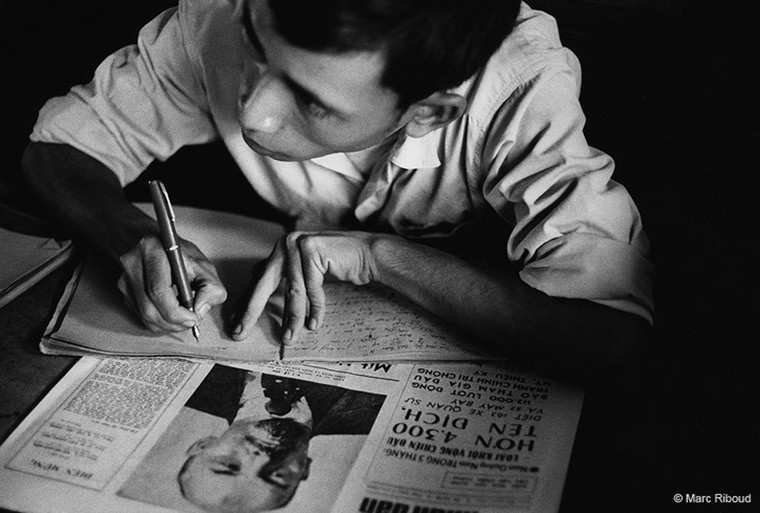 Một cán bộ ngồi bên bàn làm việc với tờ báo Nhân Dân.