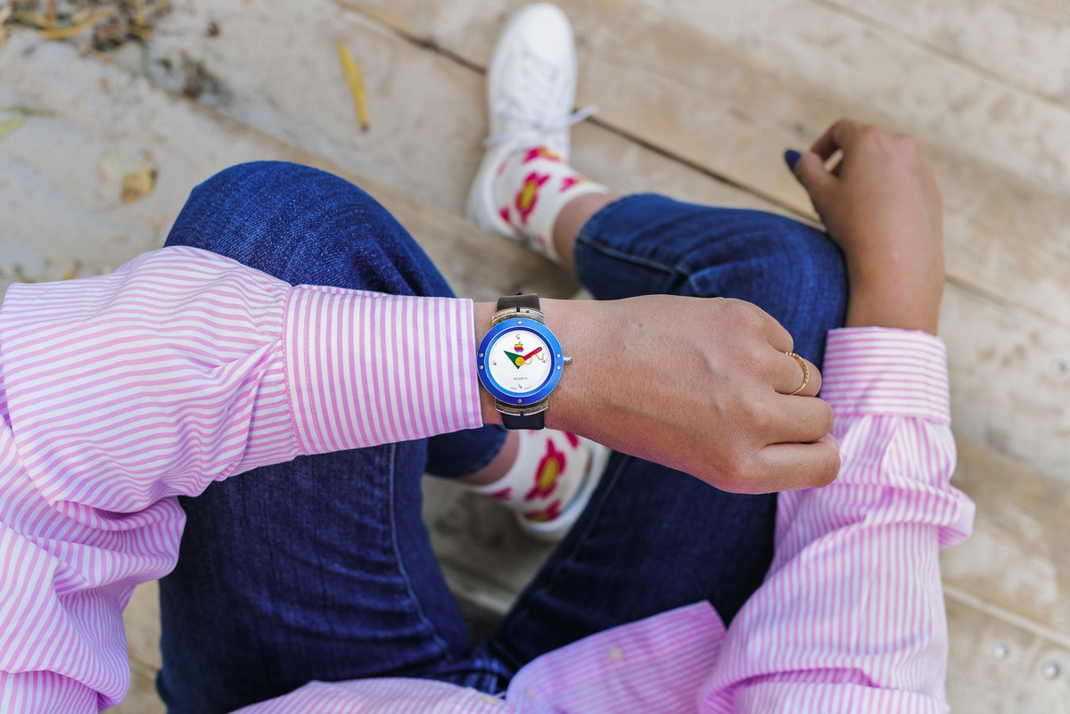 Bên dưới vị trí 12 giờ trên mặt đồng hồ là logo Apple 6 màu, kim giờ có hình tam giác màu xanh lá, kim phút hình que màu đỏ còn kim giây màu vàng, hình uốn lượn giống con rắn. Trang Hodinkee mô tả kim giây và hình tròn ở giữa đồng hồ khá giống mẫu chuột hình khúc côn cầu, được Apple ra mắt năm 1998.