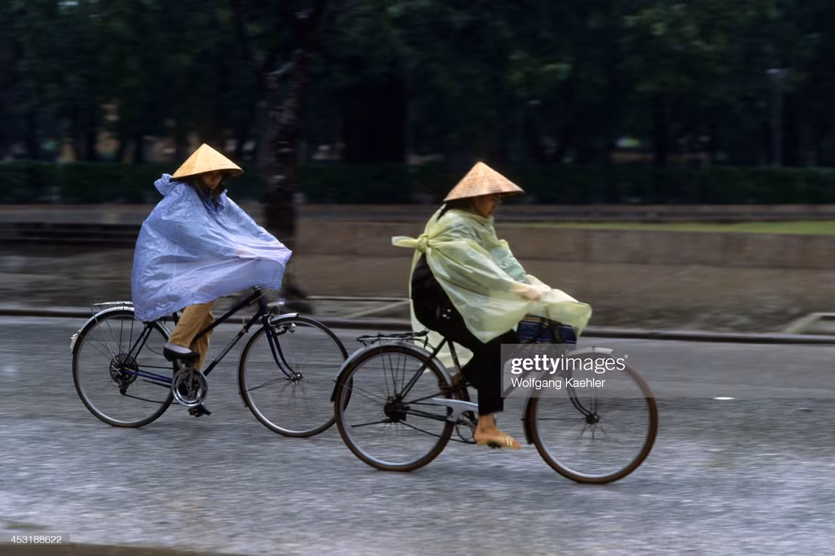 Hai người phụ nữ đạp xe dưới mưa trên đường Điện Biên Phủ, khu vực vườn hoa Lê Nin, Hà Nội.