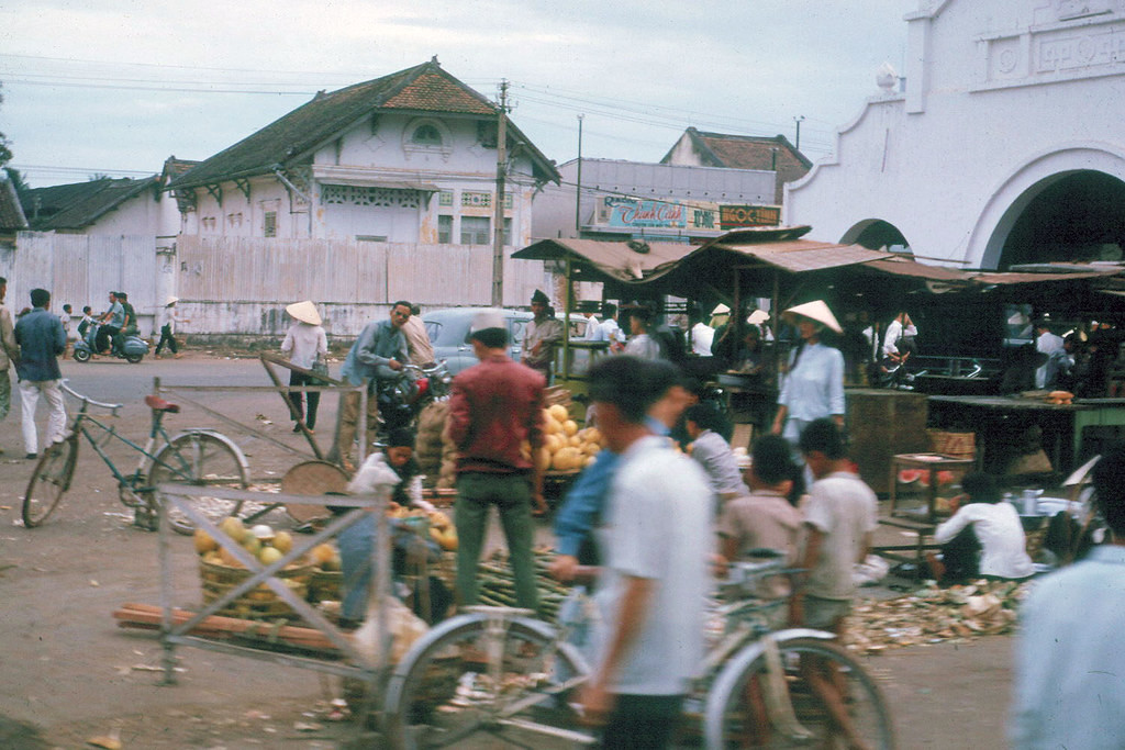 Cảnh buôn bán trước cổng chợ Thủ Đức, 1965. Ngôi nhà sau tường rào bên kia đường là trường Quân nhạc, nay là Bưu điện Thủ Đức. Ảnh: Robert Swankoski.