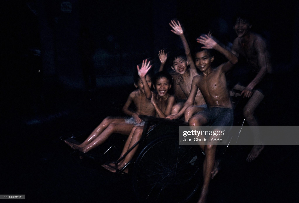 Các thiếu niên đạp xích lô, tắm mưa trên đường phố Hà Nội.