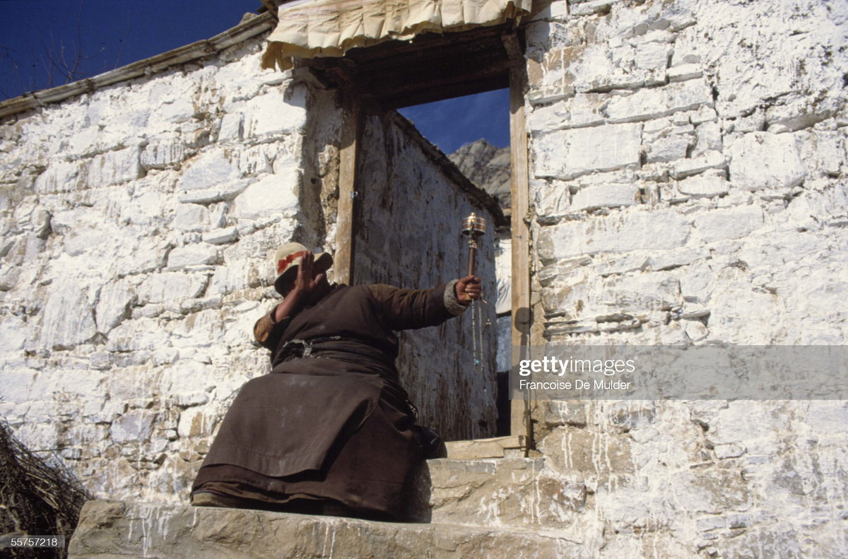 Người phụ nữ cầm bánh xe cầu nguyện trước cổng nhà ở làng Rato.