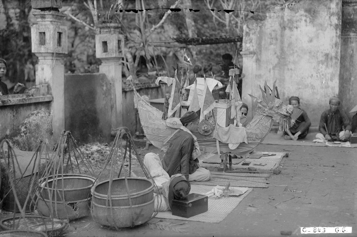 Một góc sân đền, nơi bày thúng mủng, quang gánh, đồ vàng mã. Mấy ông thầy bói trải chiếu ngồi để phục vụ khách hành hương.