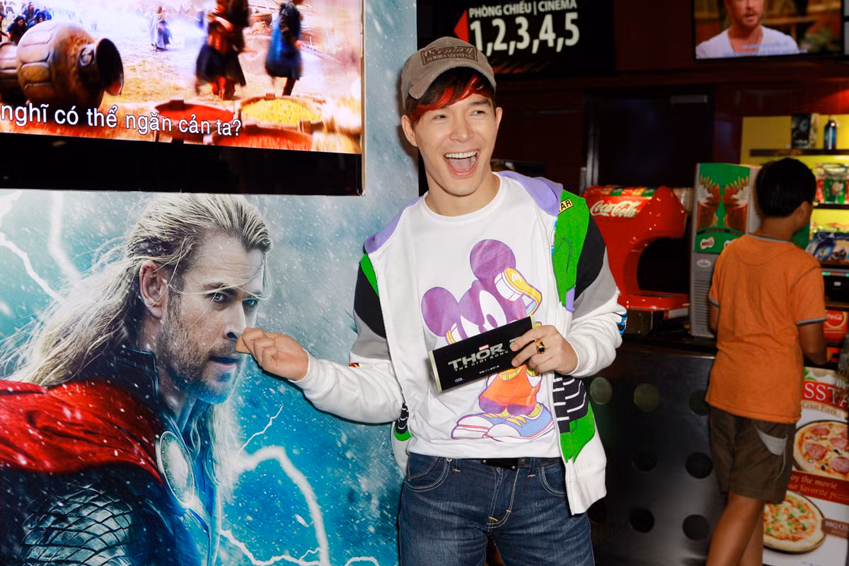 Nathan Lee mặc đồ chuột Mickey tạo dáng xì teen cạnh poster phim.