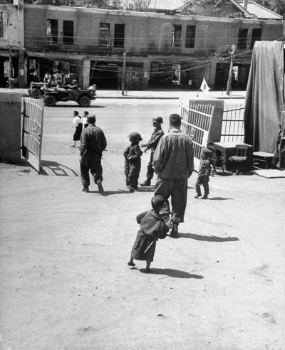 Một em bé mồ côi cầm cây gậy nghiêng mình nhìn theo bóng dáng của những người lính khi ở Seoul, Hàn Quốc.