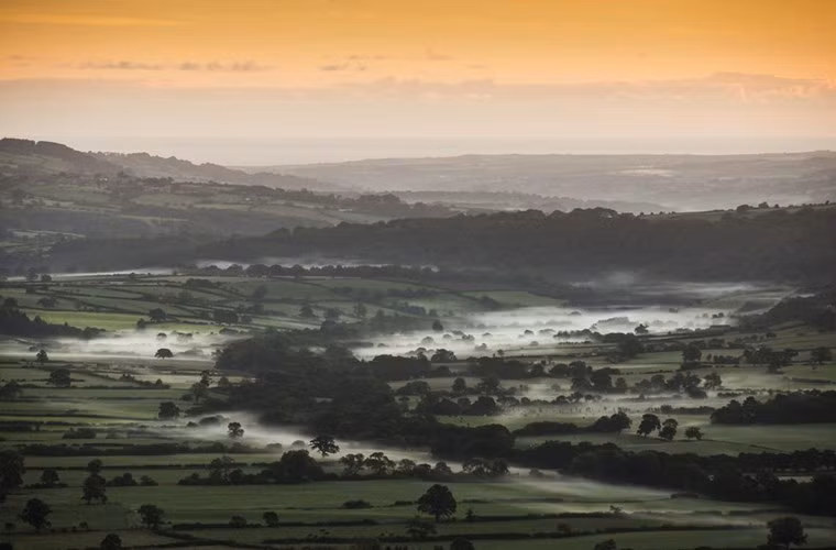 Ánh mình minh buổi sáng bắt đầu đẩy lùi màn sương thu giăng khắp thung lũng gần Goathland ở North Yorkshire Moors, Anh.