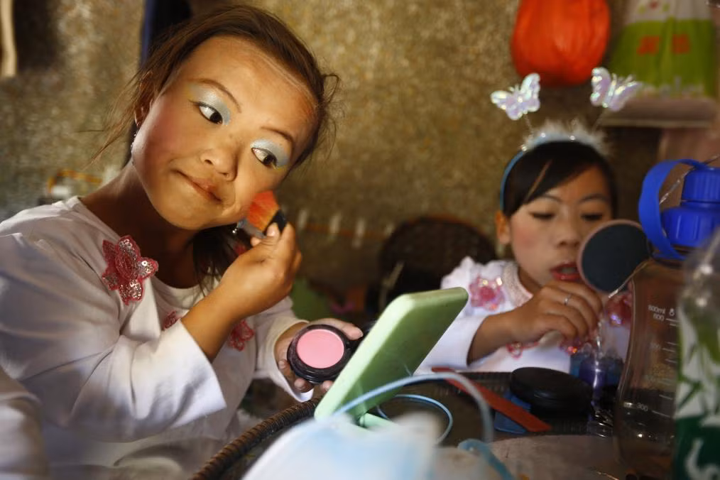 Hai thiếu nữ trong vương quốc người lùn Han Zhen Yan (trái, 19 tuổi) và cô bạn Peng Chun Song (phải, cũng 19 tuổi) đang trang điểm chuẩn bị cho một chương trình biểu diễn tạp kỹ.