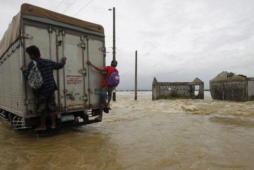 2 người đàn ông Philippines cố bám vào sau chiếc xe tải đi tránh bão lũ.
